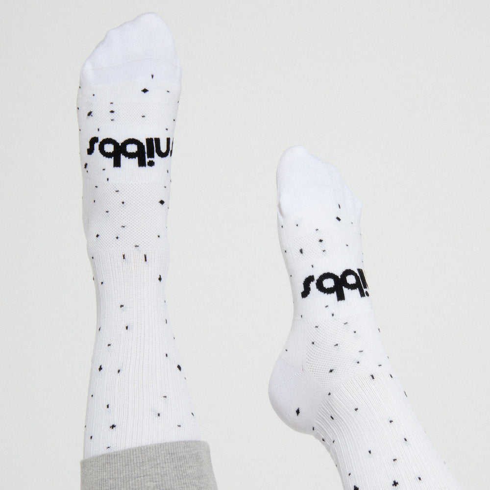 Two feet in Snibbs Compression Socks - Starry Day, white with black dots/text, designed to boost blood flow. Light gray background.