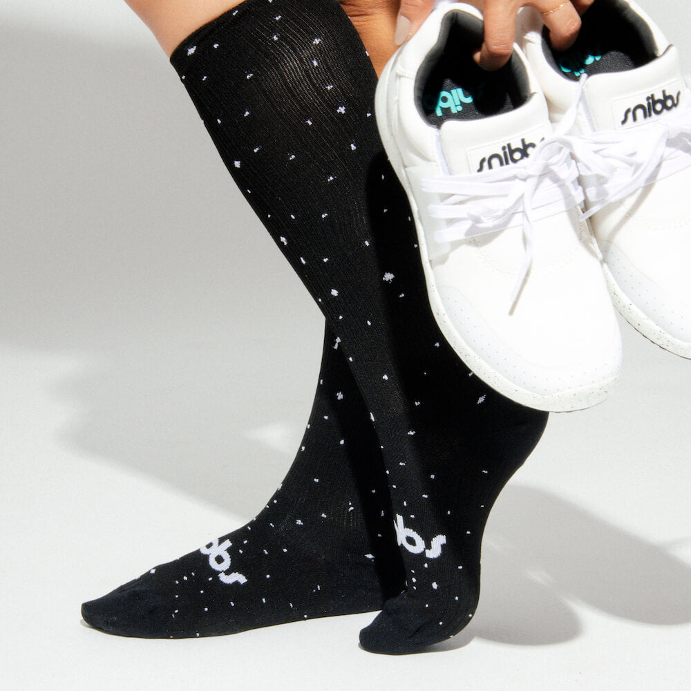 Person in Snibbs Starry Night Compression Socks holds white sneakers; plain background—perfect for relieving leg fatigue after work.