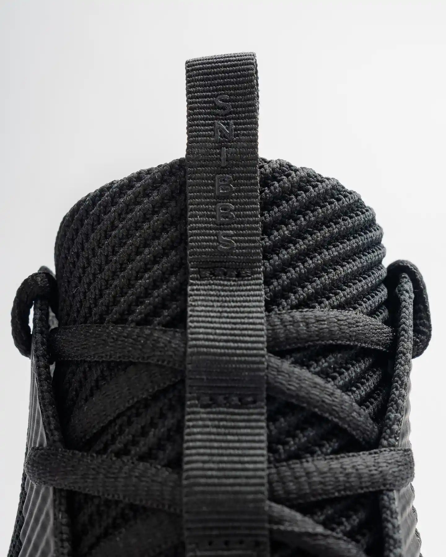 Close-up of Snibbs ROVR - WCK sneaker, black knit upper, heel pull tab labeled SNIBBS.