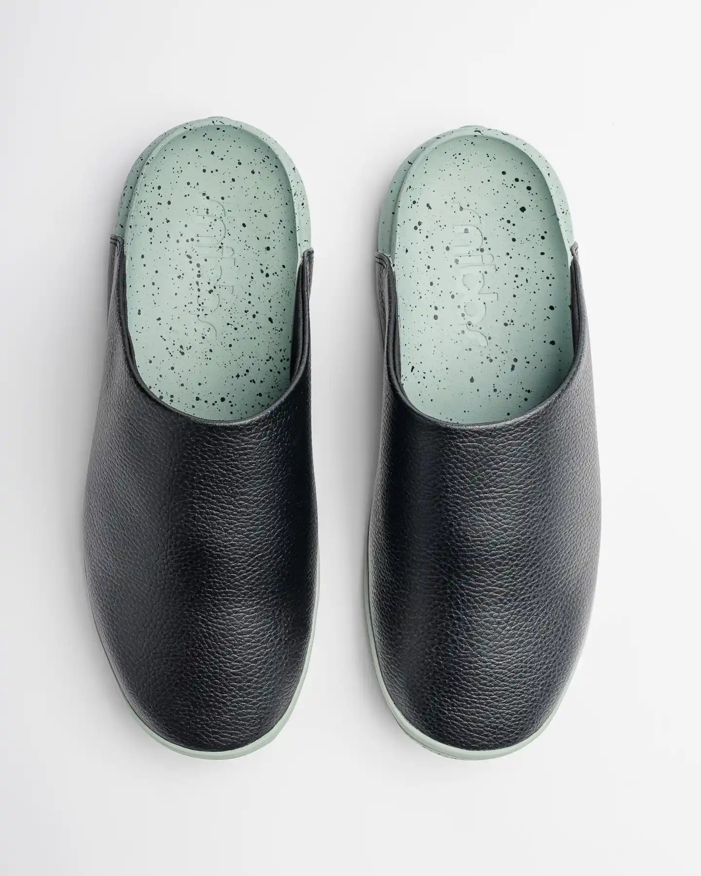 The Snibbs "The Clog - Mint Chip" is pictured from above on a white background, featuring black vegan leather uppers and insoles in a light green, speckled design.
