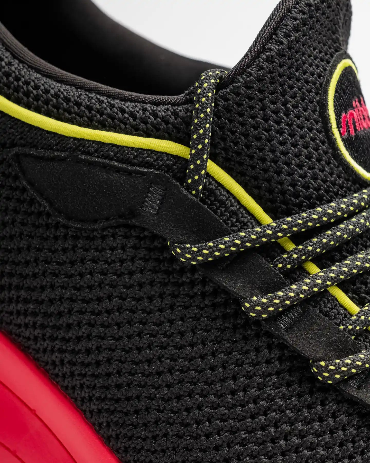 Close-up of the Snibbs Orbit - Virtual Pink athletic shoe, featuring yellow-accented laces, a yellow trim, red midsole, and textured breathable knit upper fabric. This modern shoe showcases detailed stitching, contemporary design elements, and a slip-resi