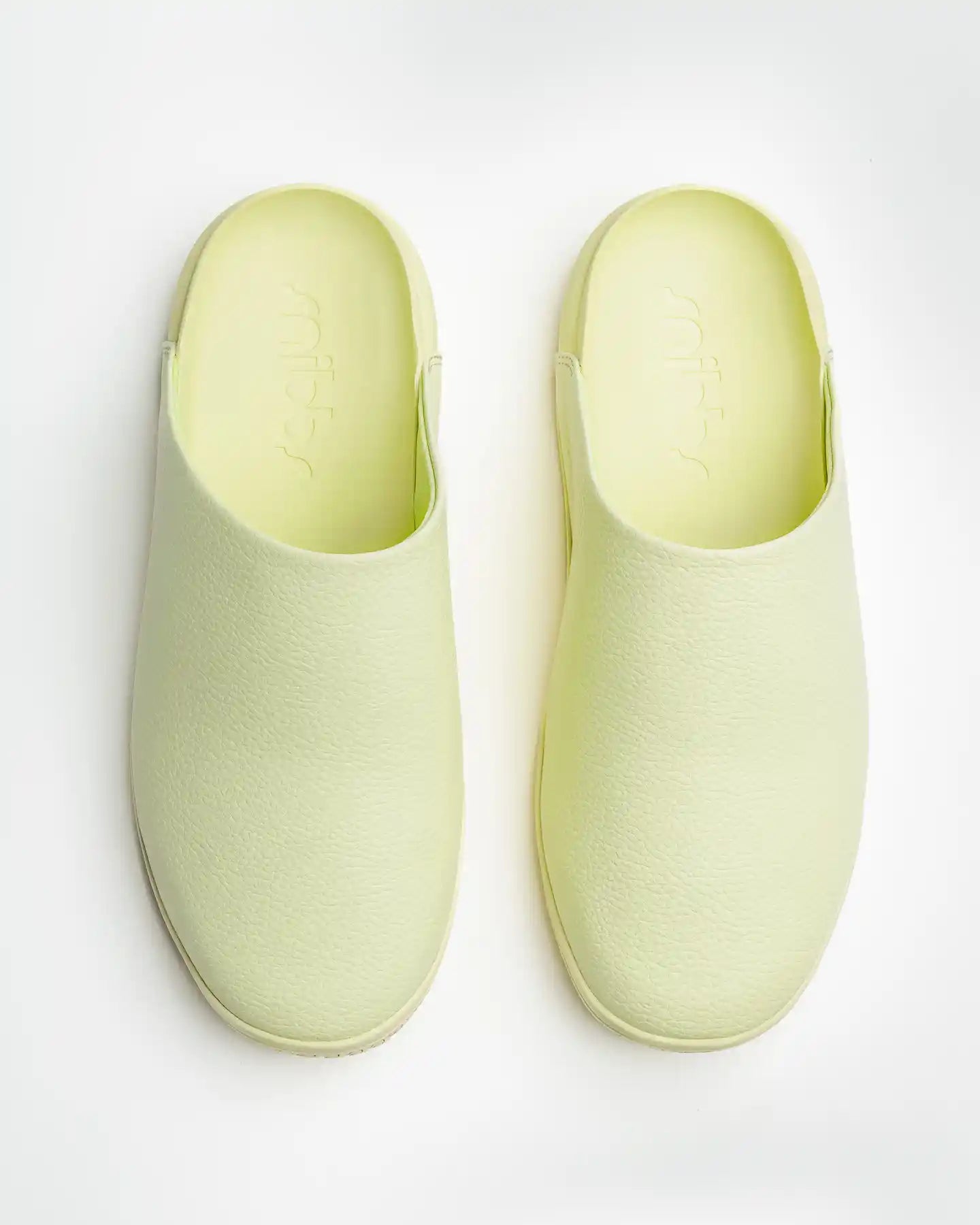 A pair of The Clog - Pistachio by Snibbs, featuring light yellow vegan leather with a textured surface, shown from above on a white background.