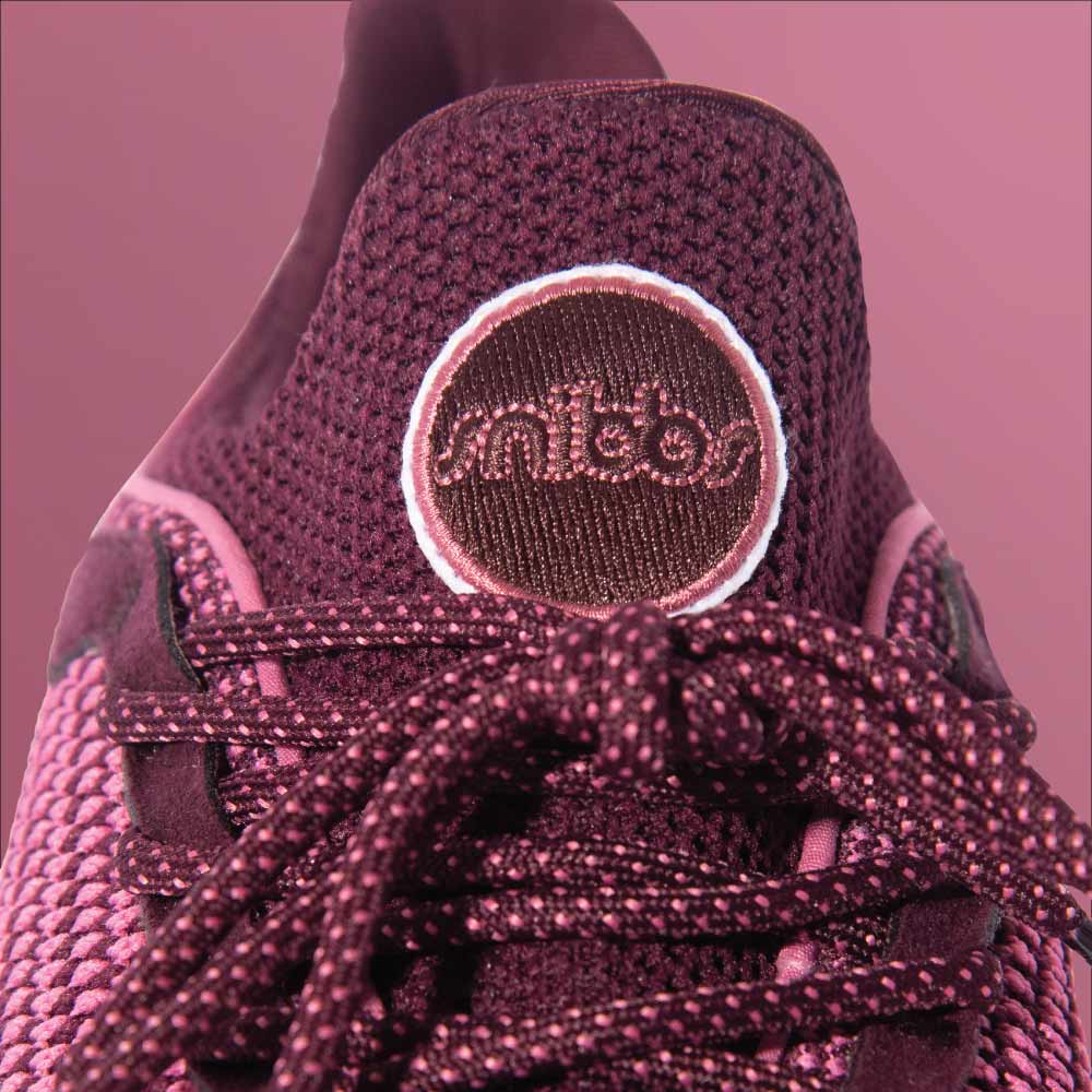 A close-up of the Snibbs Orbit - Wine Tasting: a pink and purple knit sneaker with a breathable upper, laces, and round logo on the tongue.