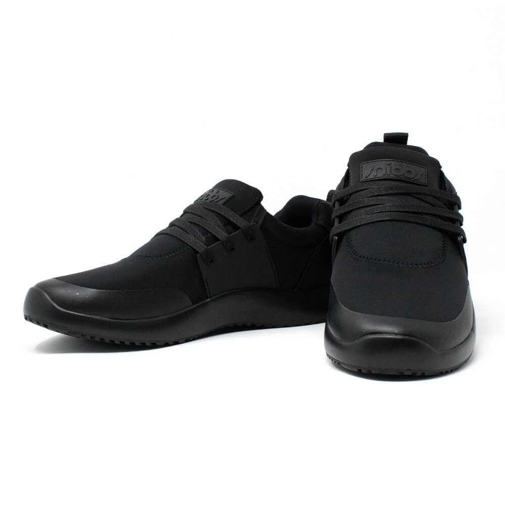 A pair of Men's Spacecloud - Eclipse Black sneakers by Snibbs, crafted from recycled materials. One shoe faces forward while the other is angled to the left, showcasing their sleek, minimalist design with laces and a textured, slip-resistant sole.