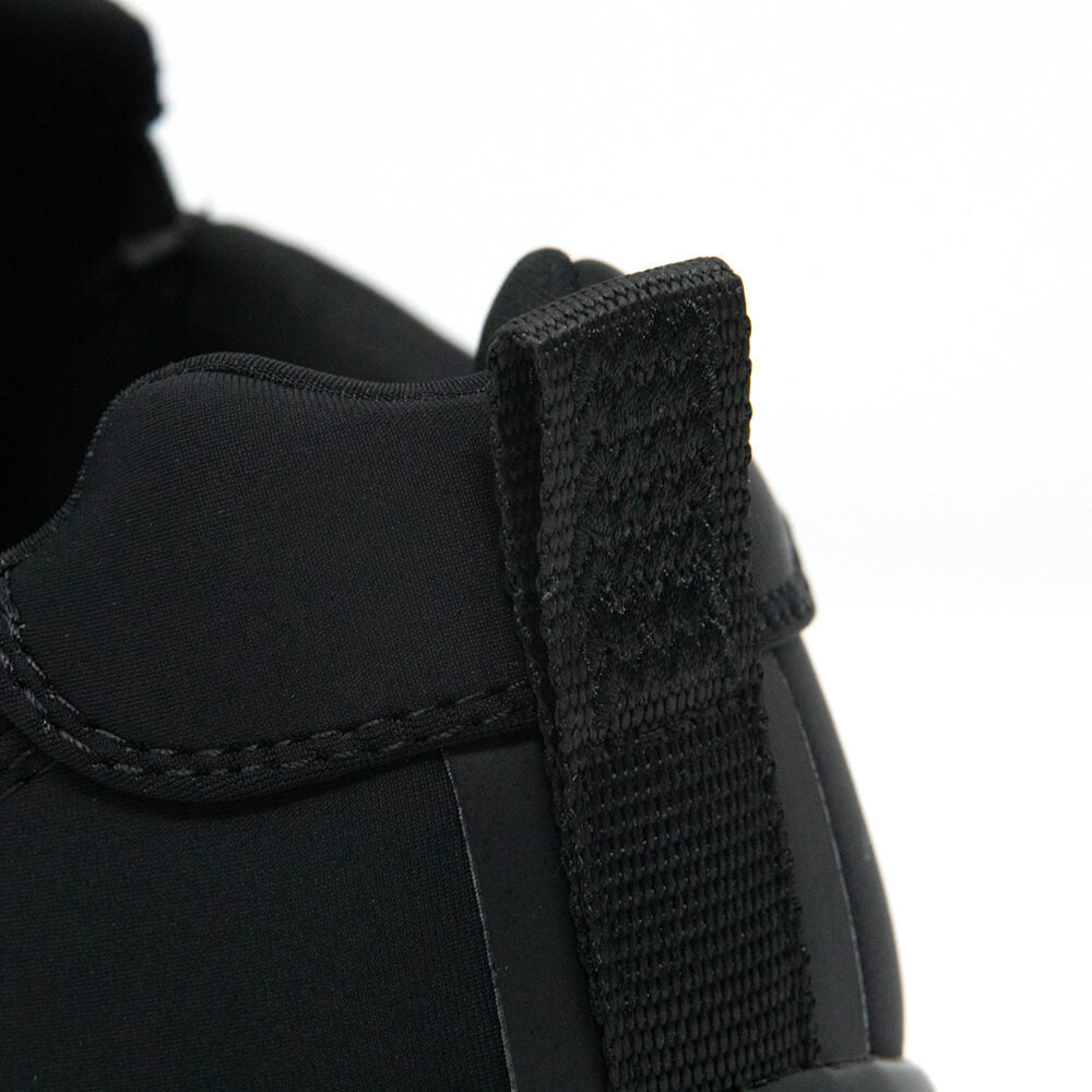 Close-up of the heel of the Snibbs Men's Spacecloud - Eclipse Black work sneaker, highlighting the sturdy fabric pull tab and detailed stitching. Crafted with recycled materials, this shoe merges eco-friendly design with lasting durability. The background