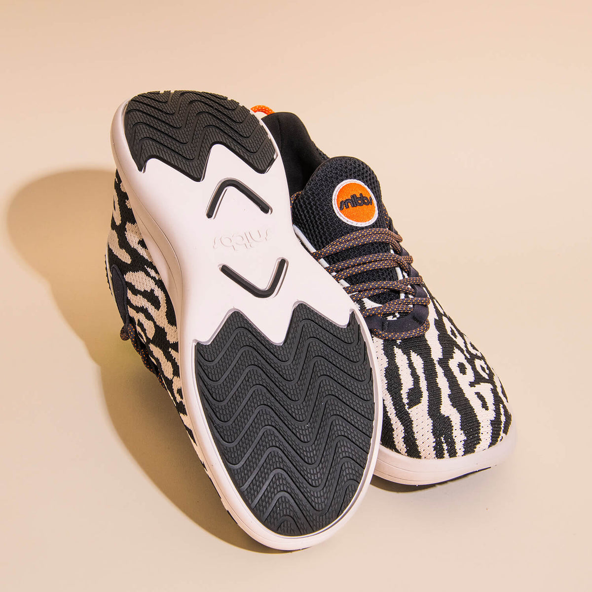 Pair of sneakers features a striking black and white snow leopard print design with solid black soles. Crafted with a breathable knit upper for enhanced comfort, one shoe stands upright while the other lies on its side, showcasing both the bold pattern an