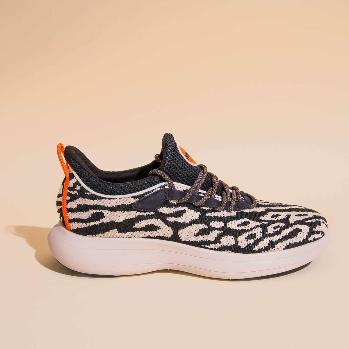 A black and white athletic sneaker featuring a bold animal print pattern, orange accents, and a thick white sole, showcased on a neutral background.