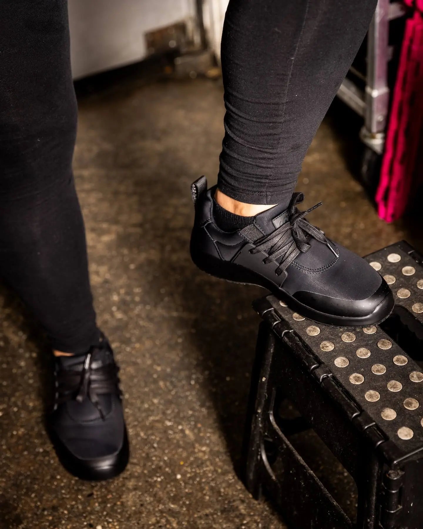 Person wearing Snibbs Spacecloud 2.0 - Tangerine stands with one foot on a black step stool with white dots on concrete.