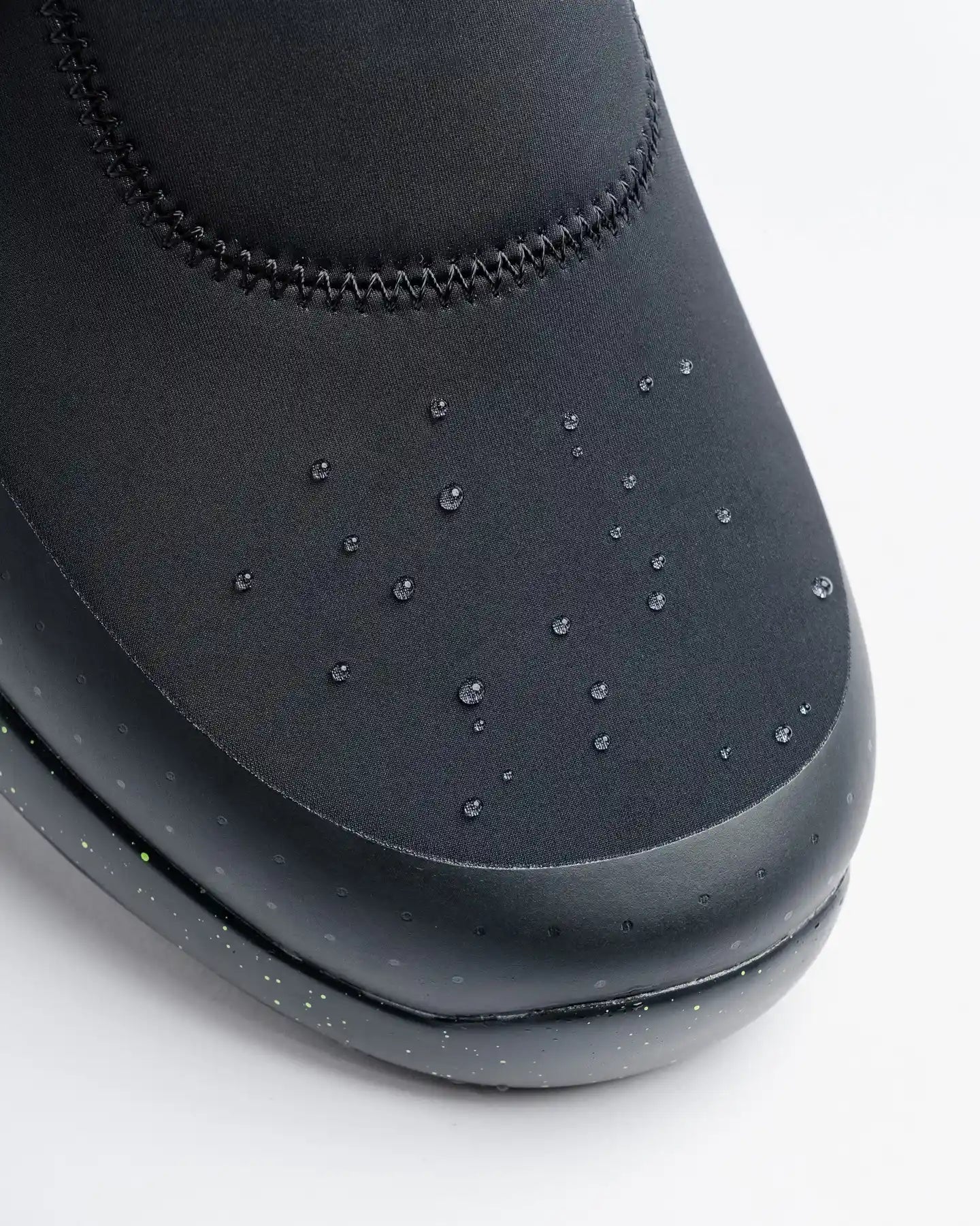 Close-up of Snibbs Spacecloud 2.0 - Lime Truck, a black water-resistant work sneaker with droplets on the toe, on light background.