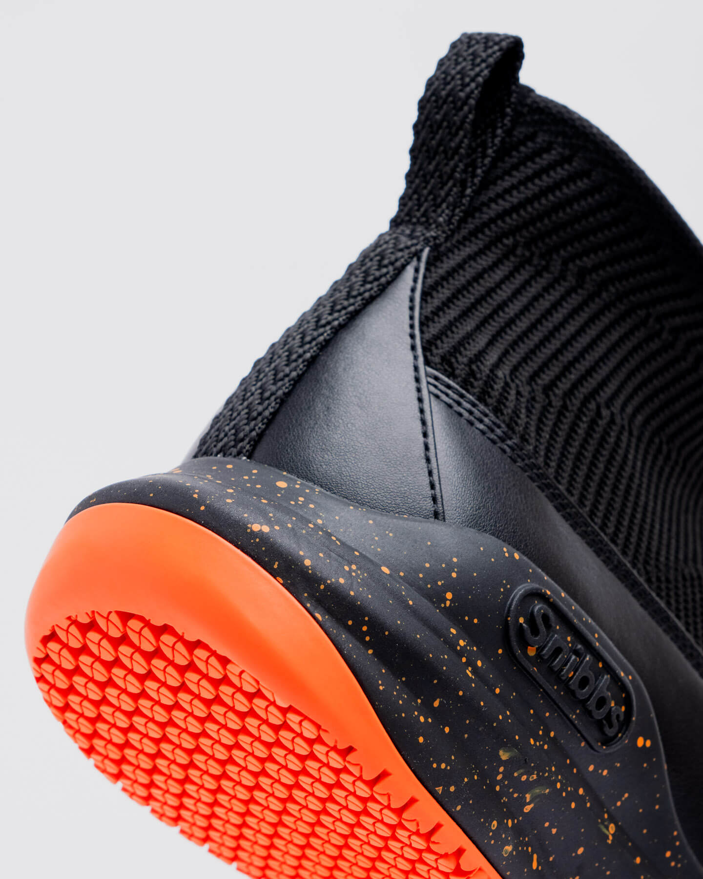Close-up of the Snibbs Pro - Tangerine heel and sole, featuring an orange non-slip outsole and yellow-speckled black midsole.