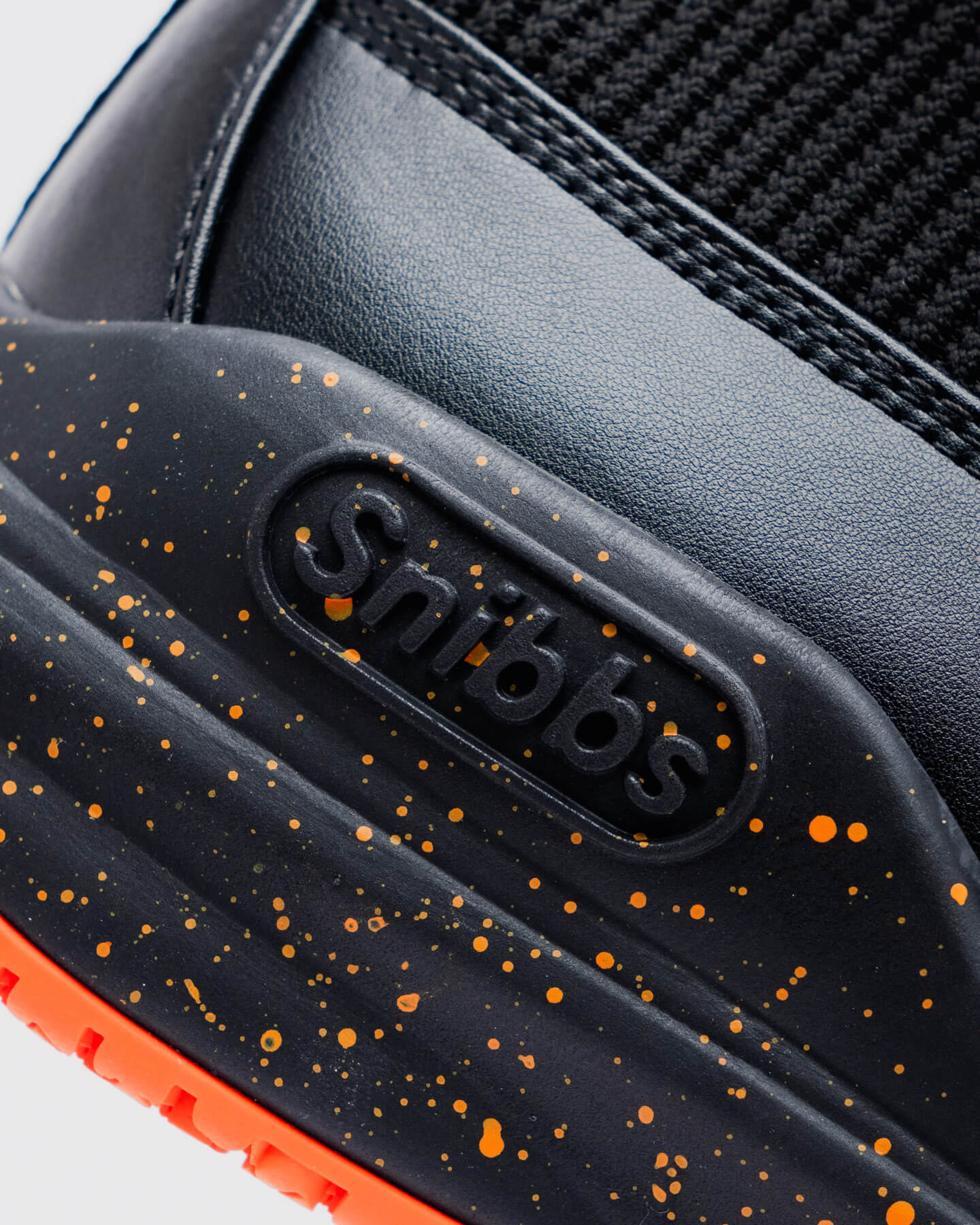 Close-up of the Snibbs Pro - Tangerine's black outsole with orange speckles, non-slip grip, and Snibbs logo on the side.