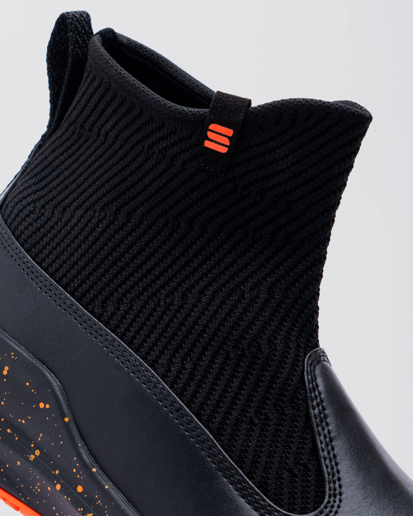 Close-up of the Snibbs Pro - Tangerine, a black high-top with knit upper, orange pull tab, and non-slip outsole for secure traction.