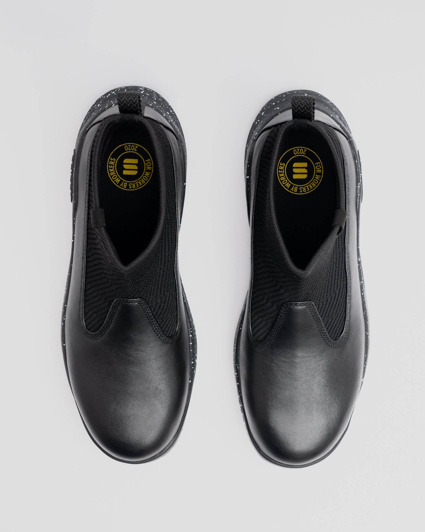 Snibbs Pro - Black Speckle slip-ons with elastic uppers and cushioned speckled soles, top view on a light gray background.