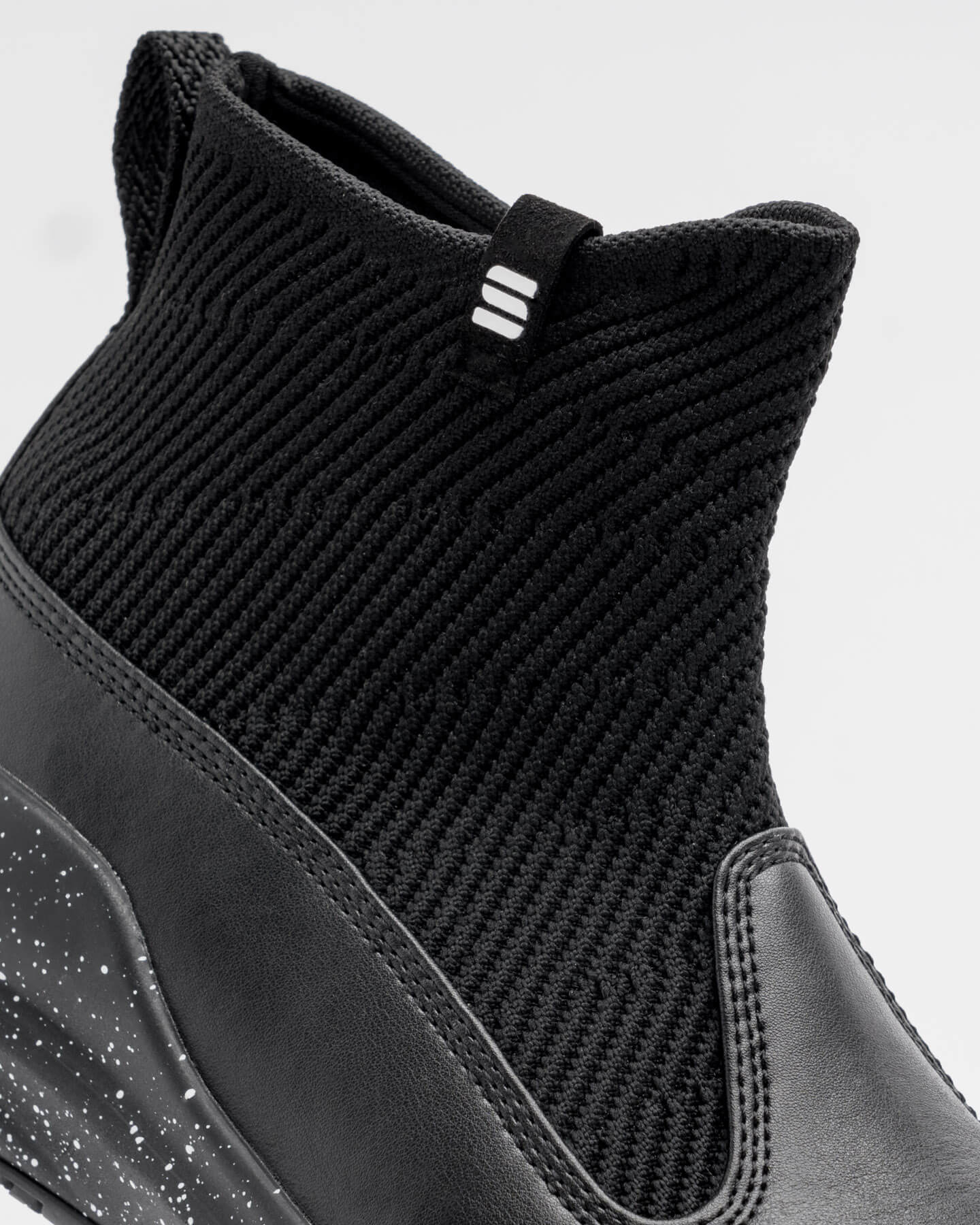 Close-up of Snibbs Pro - Black Speckle high-top with ribbed knit, leather details, and non-slip rubber outsole for traction.