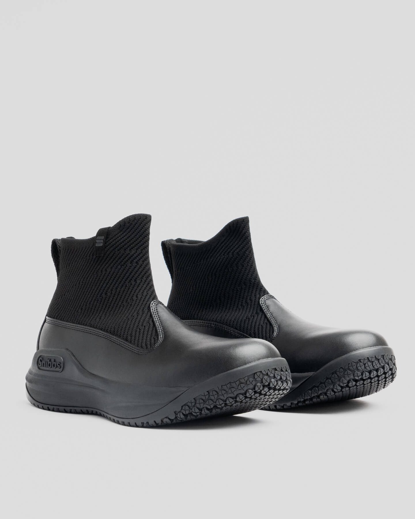 Snibbs Pro - Eclipse Black: black ankle-high boots with a premium knit upper and textured rubber soles on a light gray background.