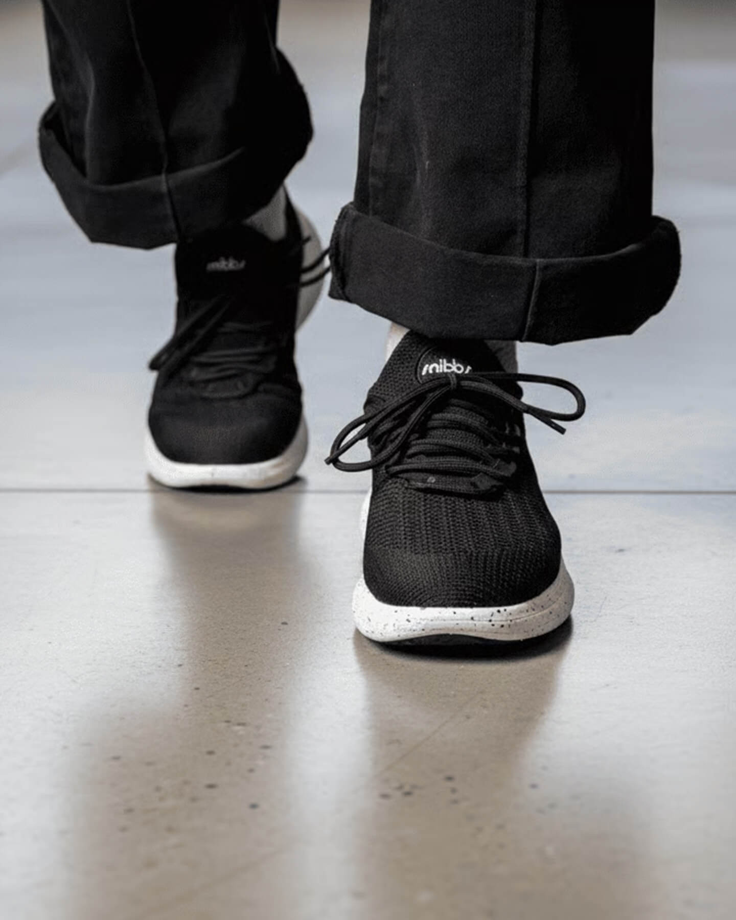 A person in Snibbs Orbit - Nebula Blue sneakers and black pants walks on a smooth, light-colored floor.