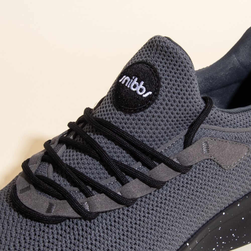 Close-up of Snibbs Orbit - Charcoal, featuring black laces, slip-resistant sole, mesh texture, and a circular logo on the tongue.