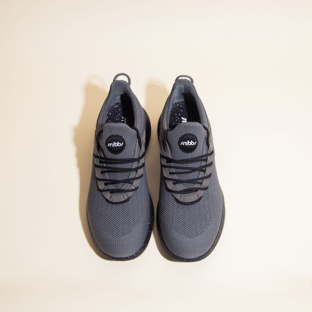A top view of Snibbs Orbit - Charcoal sneakers with black laces and a breathable knit upper on a plain light background.