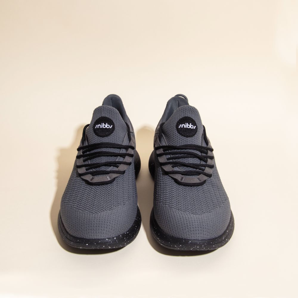 Snibbs Orbit - Charcoal athletic shoes with a breathable knit upper and slip-resistant soles are shown side by side on a beige background.