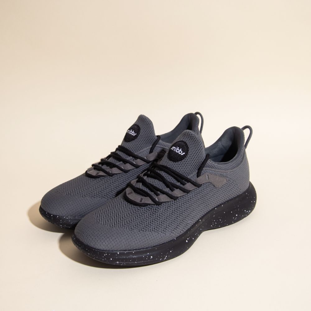 Snibbs Orbit - Charcoal athletic sneakers with black speckled, slip-resistant soles are displayed on a light surface.