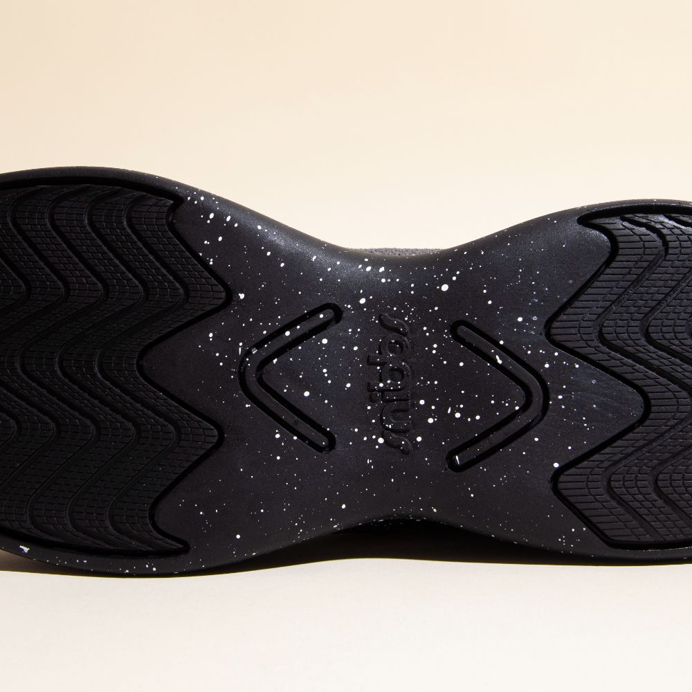Close-up of Orbit - Charcoal’s slip-resistant sole by Snibbs, with white speckles, textured patterns, and "snibbs" embossed in the center.