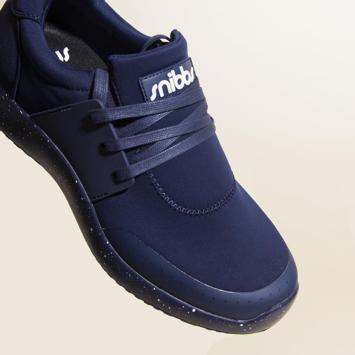 A close-up of the Snibbs Women's Spacecloud sneaker in Nebula Blue, showcasing dark laces and speckled detailing on its slip-resistant sole, with "snibbs" displayed on the tongue, all set against a light background.