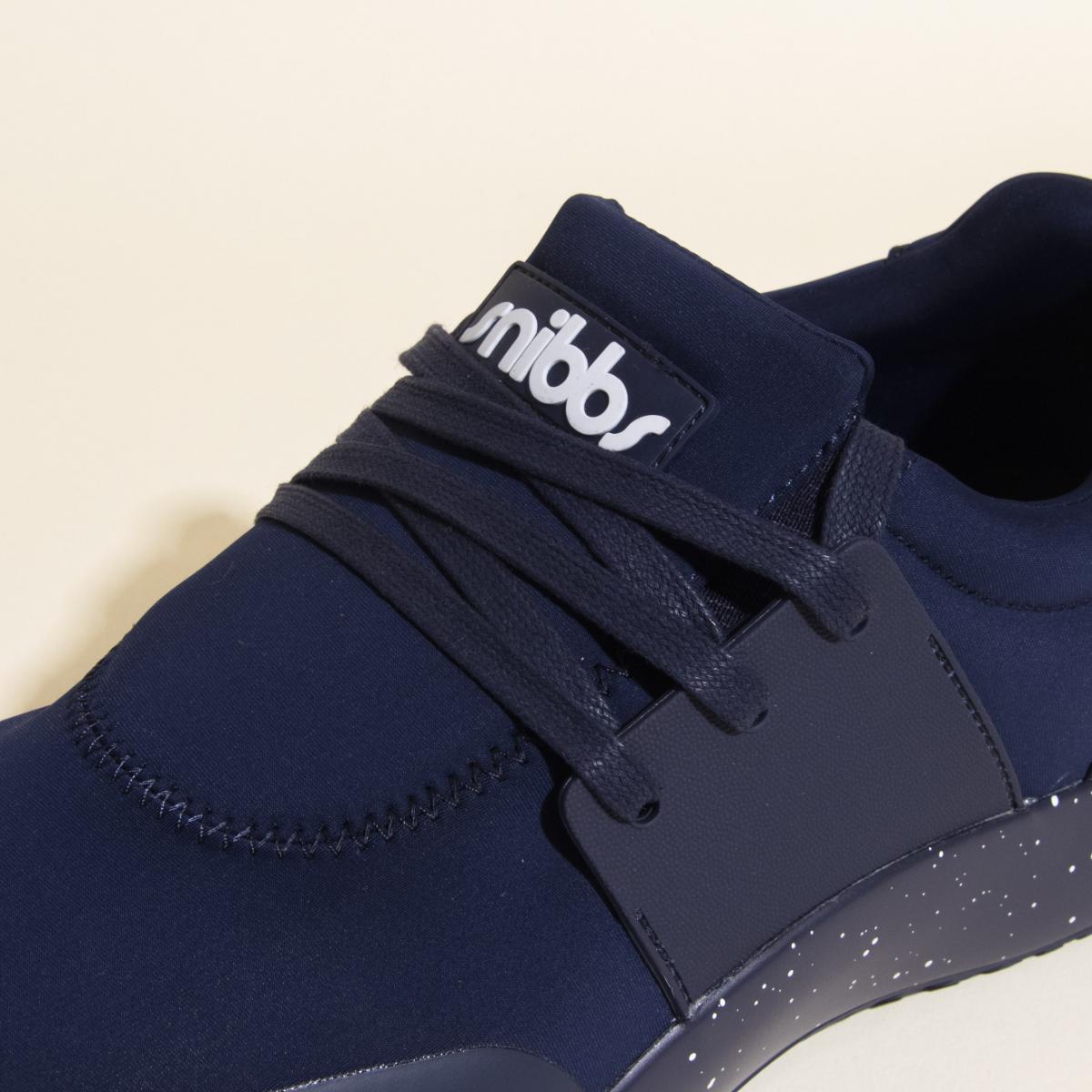 A close-up of the Snibbs Women's Spacecloud in Nebula Blue, a vegan work sneaker featuring dark laces, a black and white speckled slip-resistant sole, and the Snibbs logo on the tongue.