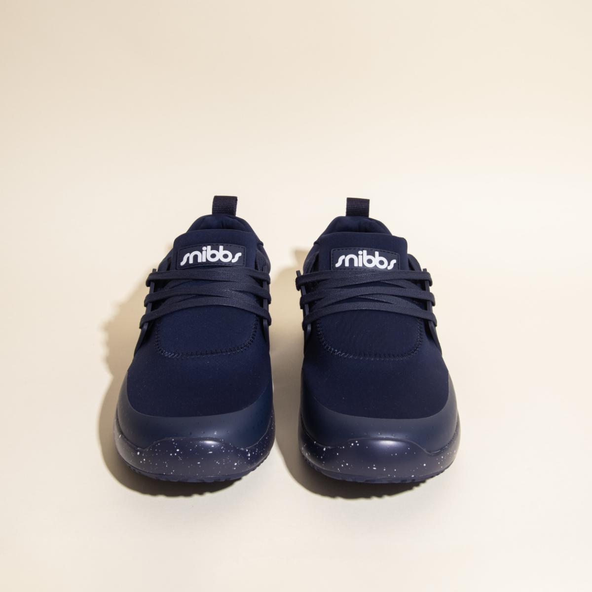 A pair of Snibbs Women's Spacecloud sneakers in Nebula Blue with dark, slip-resistant soles featuring white speckles, shown from the front against a plain beige background.